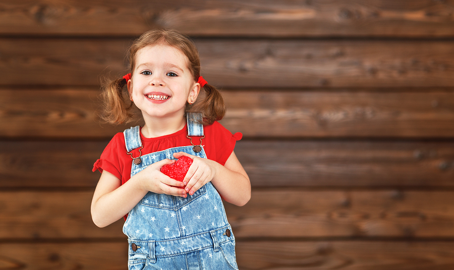 happy laughing child girl with heart Valentine's Day wooden background
