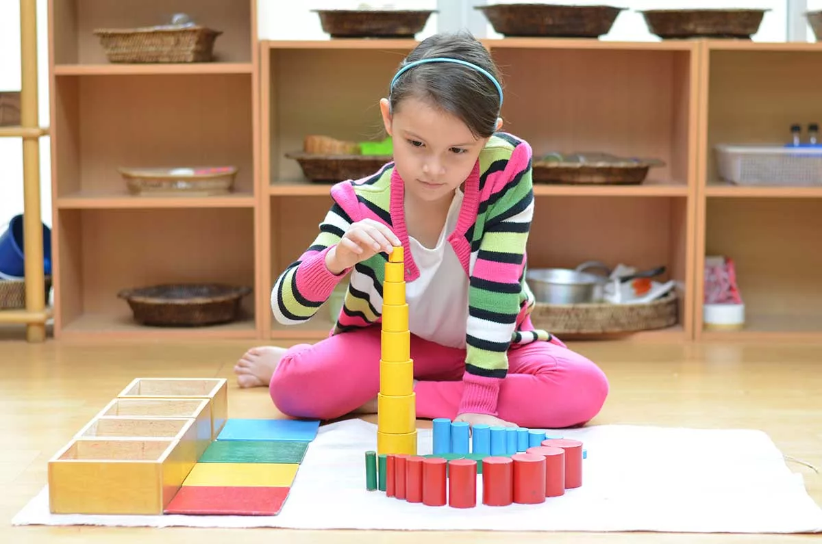 young girl with striped sweater using Montessori toys sitting on carpet