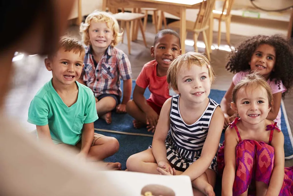 young school aged children sitting on carpet smiling at the presenter